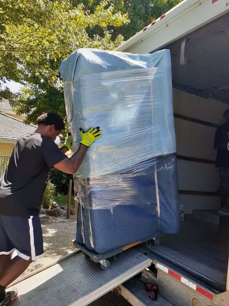 Professional movers moving wrapped furniture down a ramp into a moving truck.