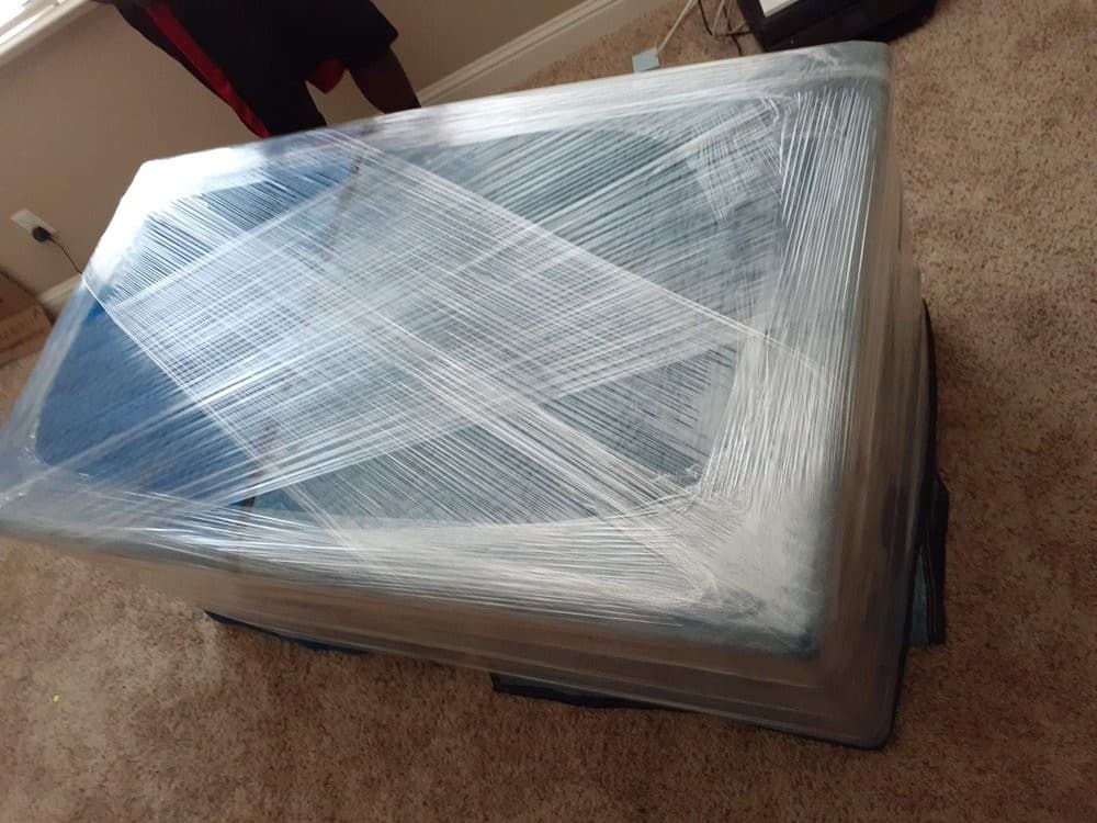 Sacramento movers wrapping a large sofa for transport with thick moving blankets and stretch wrap.